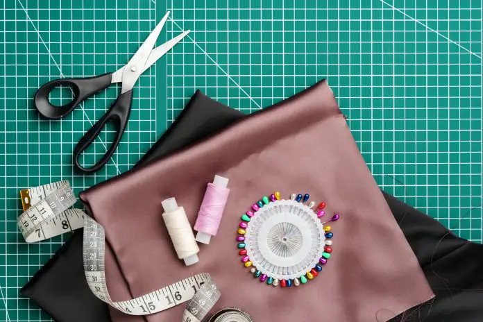 Craft supplies for sewing on a green cutting mat with fabric, scissors, and measuring tools